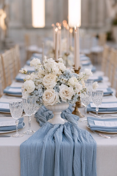 Dusty Blue Wedding Decor: Florals, Table Settings and Reception Styling 4 Elegant wedding tablescape with dusty blue runner, white floral centerpiece, crystal glassware, and taper candles on a banquet table.