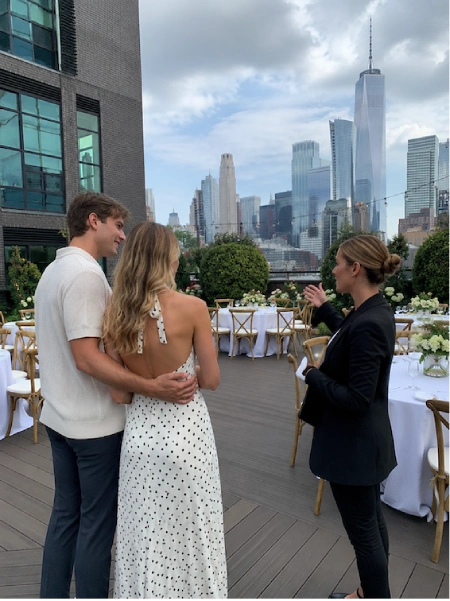 What to discuss before planning a wedding 2 Wedding planner tours rooftop venue with engaged couple overlooking Manhattan skyline while discussing reception setup