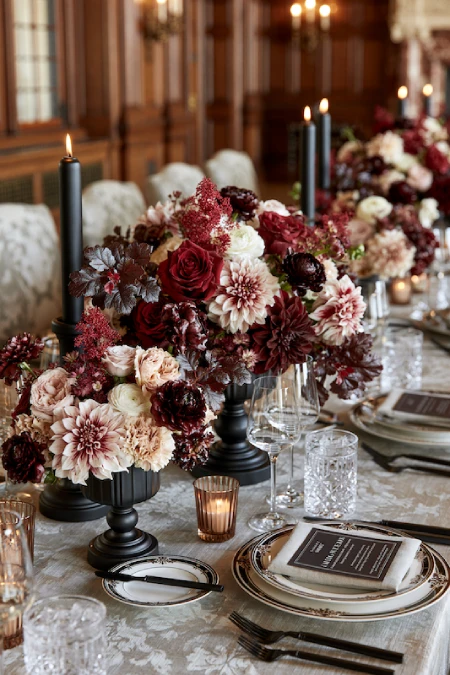 Moody burgundy and blush floral centerpieces with black candlesticks on an elegant fall wedding reception table