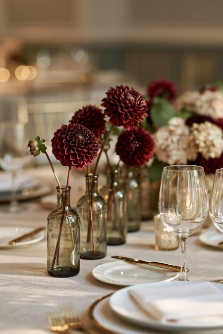 Burgundy dahlia bud vases create a simple, elegant wedding centerpiece with candlelight on a round reception table