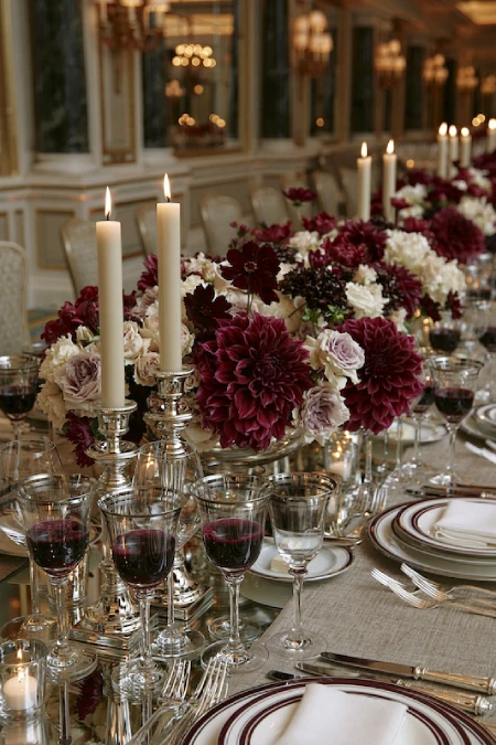 Burgundy dahlia wedding centerpiece with silver candlesticks, ivory blooms, and candlelight on an elegant reception table