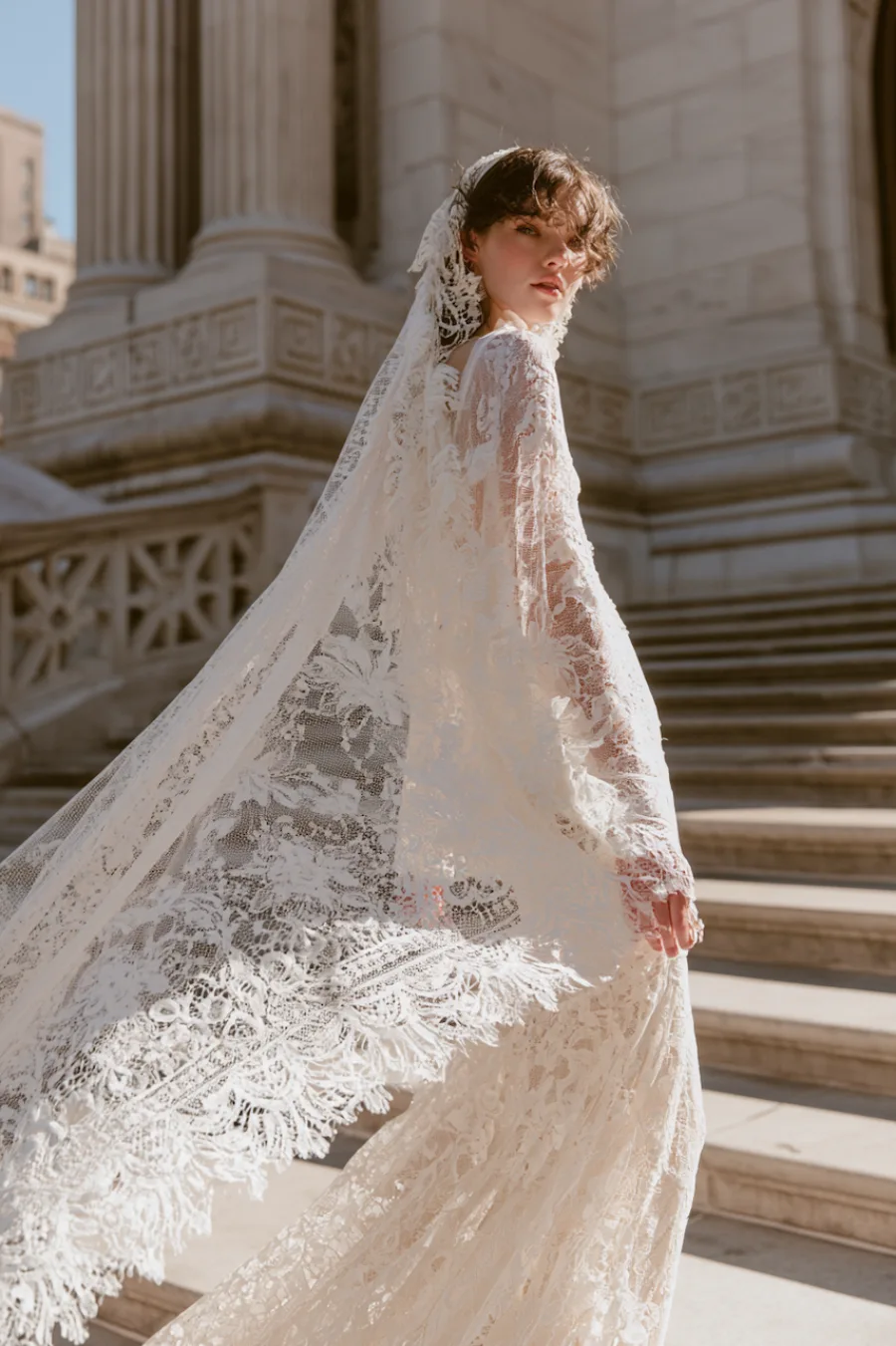 12 Timeless Lace Wedding Dress Styles We Love 5 Bride in a Chantilly lace wedding dress with matching lace veil flowing across grand stone steps in elegant outdoor portrait