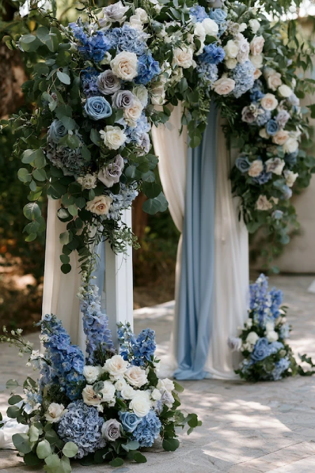 Dusty Blue and Sage Green Wedding Decor: The Color Pairing That Has Brides Completely Obsessed Right Now 7 Dusty blue and sage green wedding ceremony arch with cascading roses, hydrangeas, eucalyptus, and soft ivory drapery.