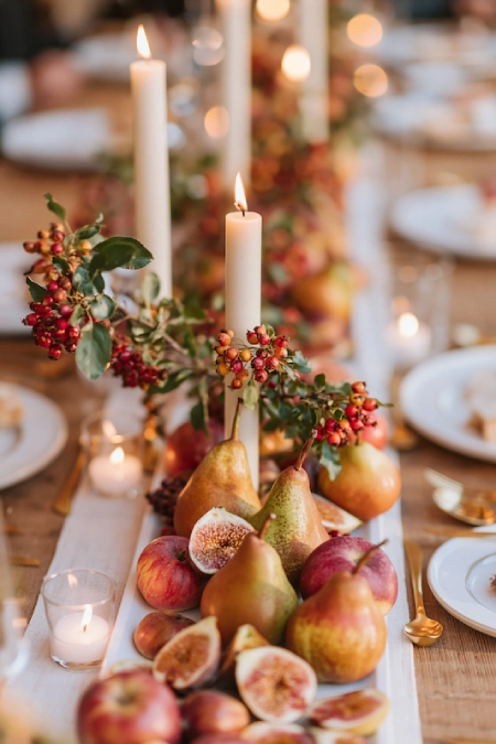 Fall wedding centerpiece with pears, figs, berries, taper candles, and seasonal fruit styled on a rustic reception table