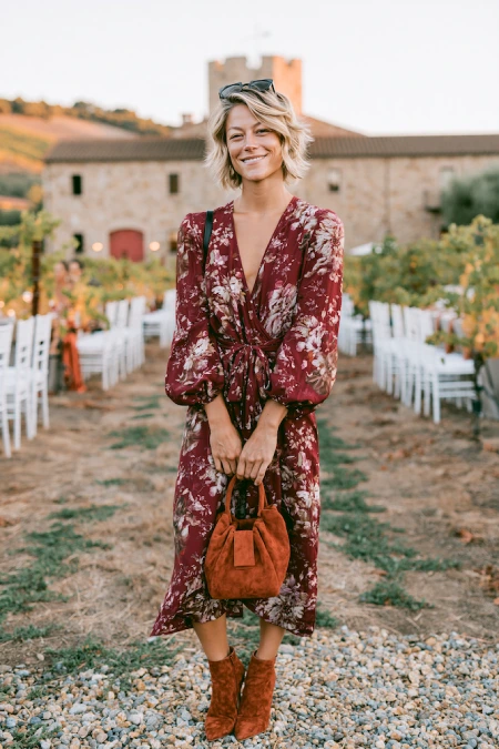 Woman in a burgundy floral midi dress and suede boots at a vineyard rehearsal dinner with rustic fall style