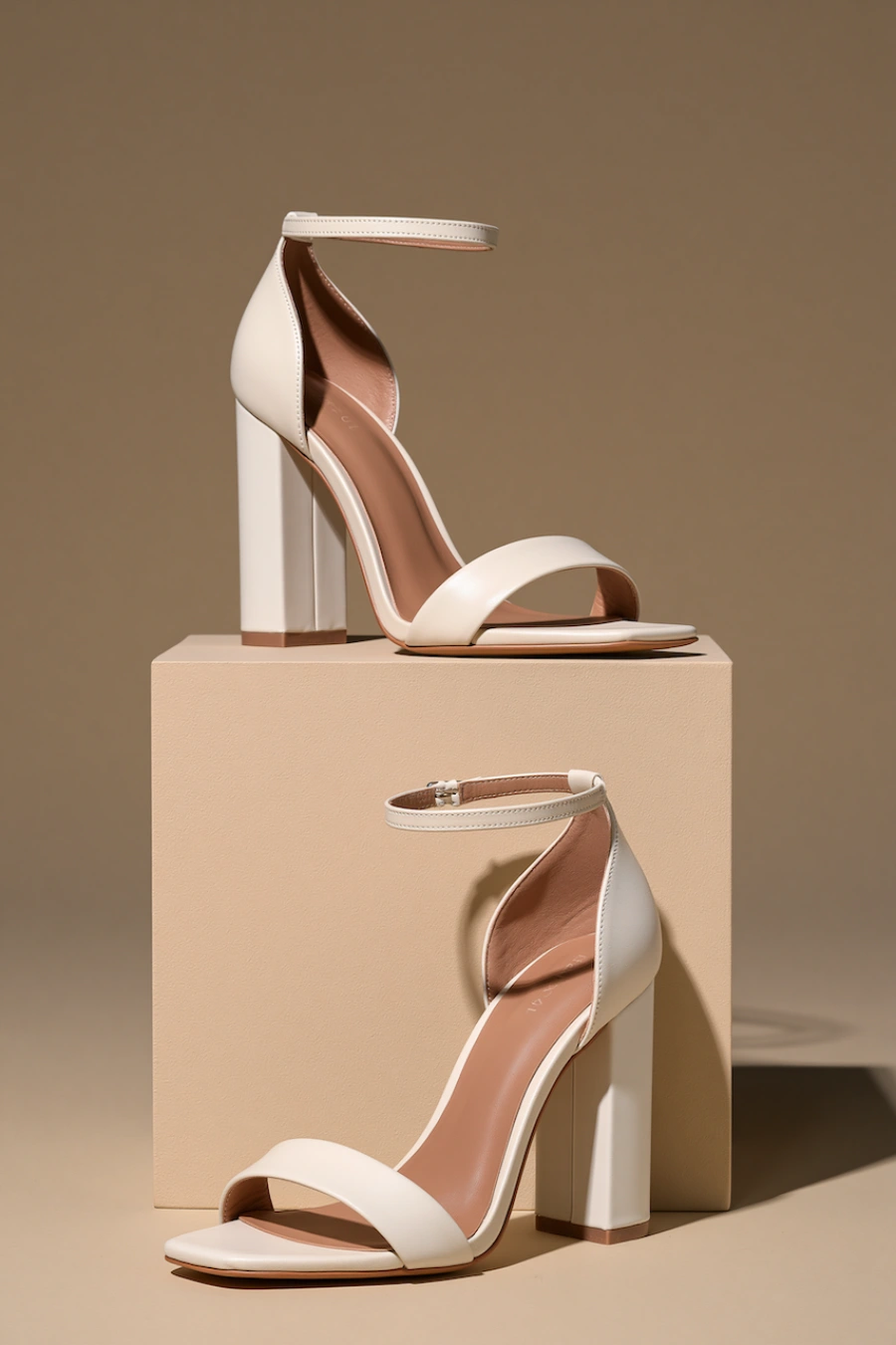 Wedding Shoes for the Bride: 27 Beautiful Ideas That Balance Style and Comfort 10 Ivory block heel bridal sandals with ankle straps and open toes displayed on pedestal blocks in a minimalist studio setting