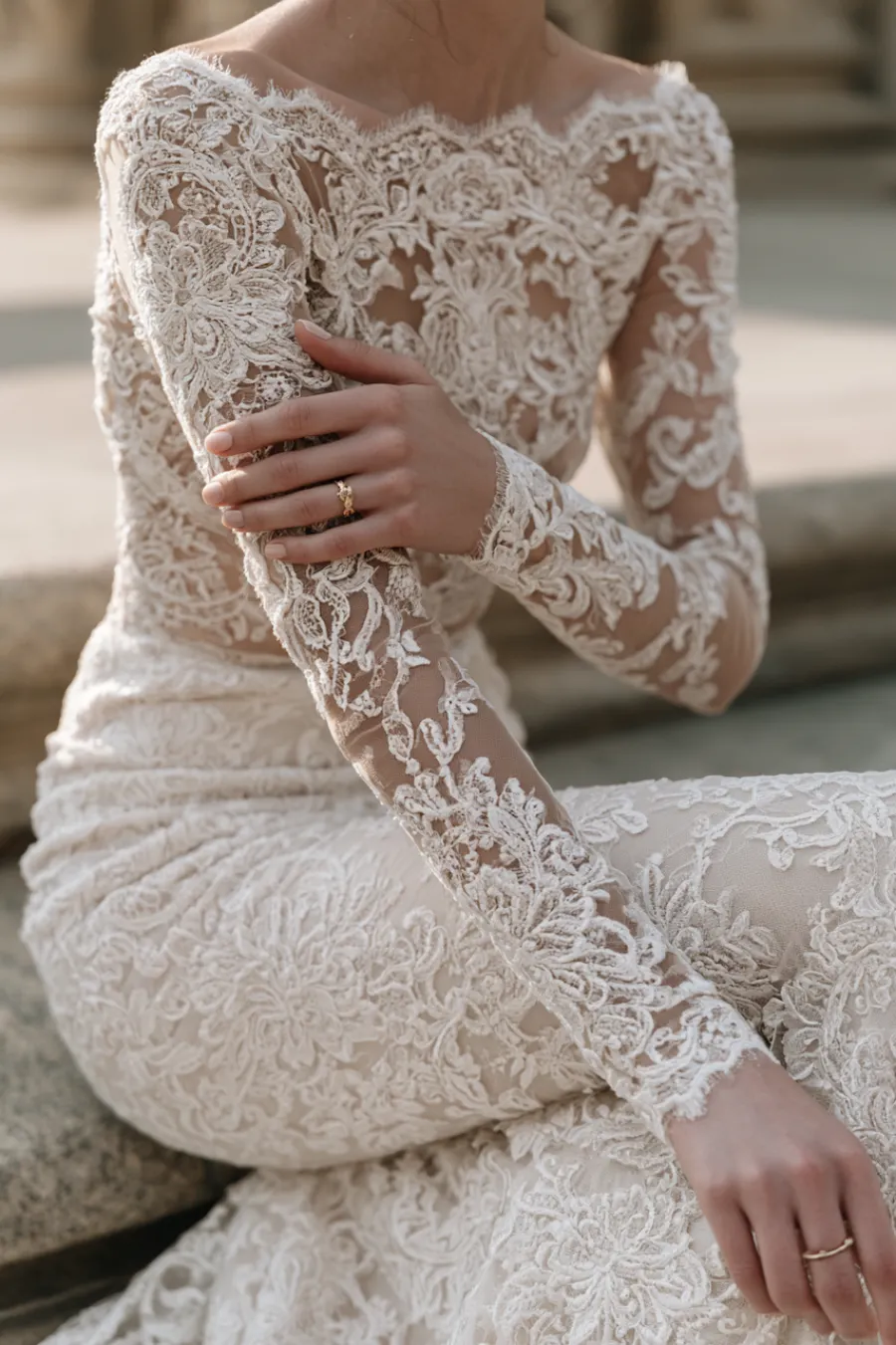 12 Timeless Lace Wedding Dress Styles We Love 3 Bride wearing a fitted lace wedding dress with illusion long sleeves and floral embroidery, highlighting intricate bridal details