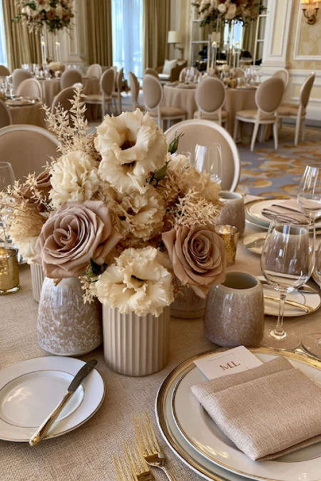 Neutral wedding centerpiece with taupe roses, ivory blooms, and ceramic bud vases on an elegant ballroom reception table
