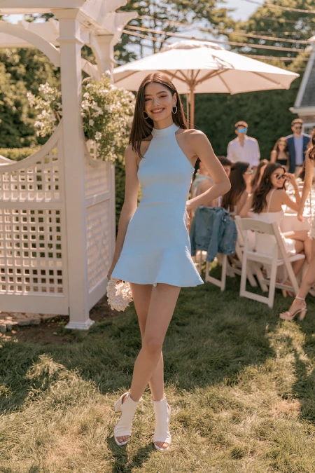 Woman in a pale blue mini dress at an outdoor garden rehearsal dinner with a playful and modern summer look