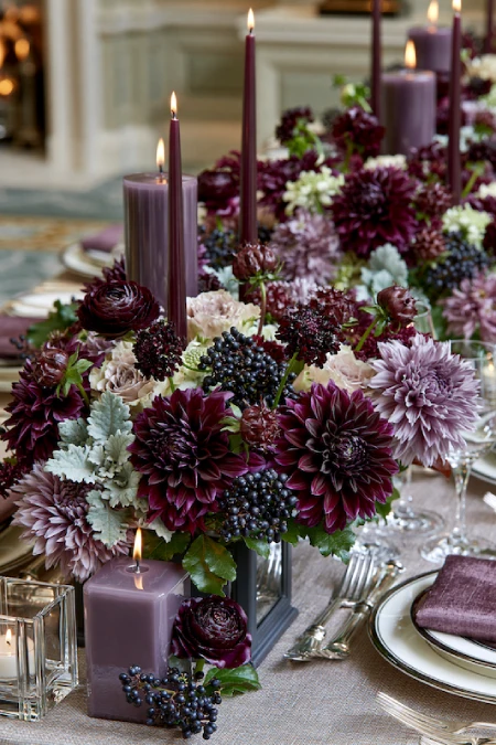 Moody plum and burgundy dahlia centerpiece with purple candles, berries, and lush florals on a luxury wedding table