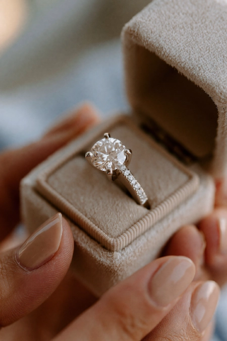 Proposal Ideas: 40 Ways to Pop the Question She'll Never Stop Talking About 14 Close-up of a round diamond engagement ring in an open velvet ring box held in hands with a soft neutral manicure