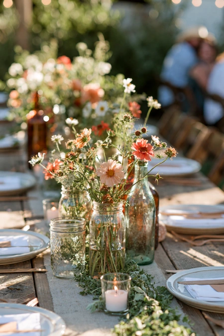 Rehearsal Dinner Centerpieces That Understood the Assignment: Easy Ideas for the Night Before the Big Night 4 Rustic backyard rehearsal dinner centerpiece with wildflowers in glass jars and soft candlelight on wood tables
