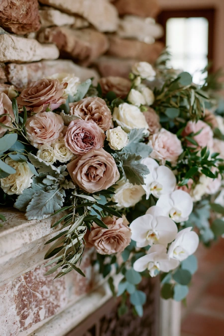 Sage Green and Terracotta Wedding: The Earthy Duo That Understood the Assignment 3 Wedding fireplace mantel with blush roses, white orchids, eucalyptus, and lush greenery in a rustic stone reception venue