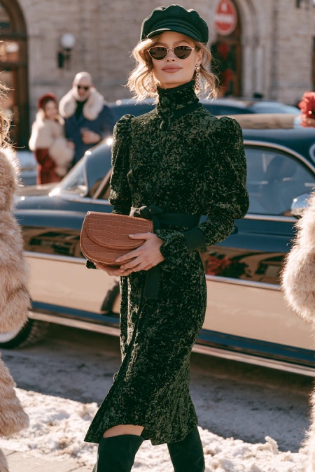 Woman in a black velvet dress with boots and beret styled for a chic winter rehearsal dinner in the city