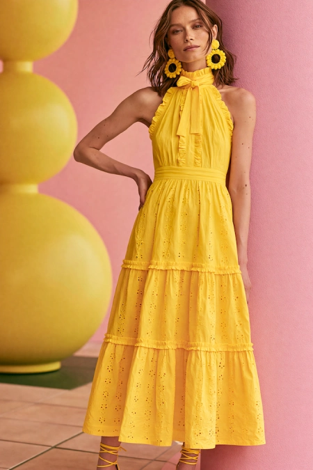 Woman in a vibrant yellow midi dress with statement earrings styled for a cheerful summer rehearsal dinner look