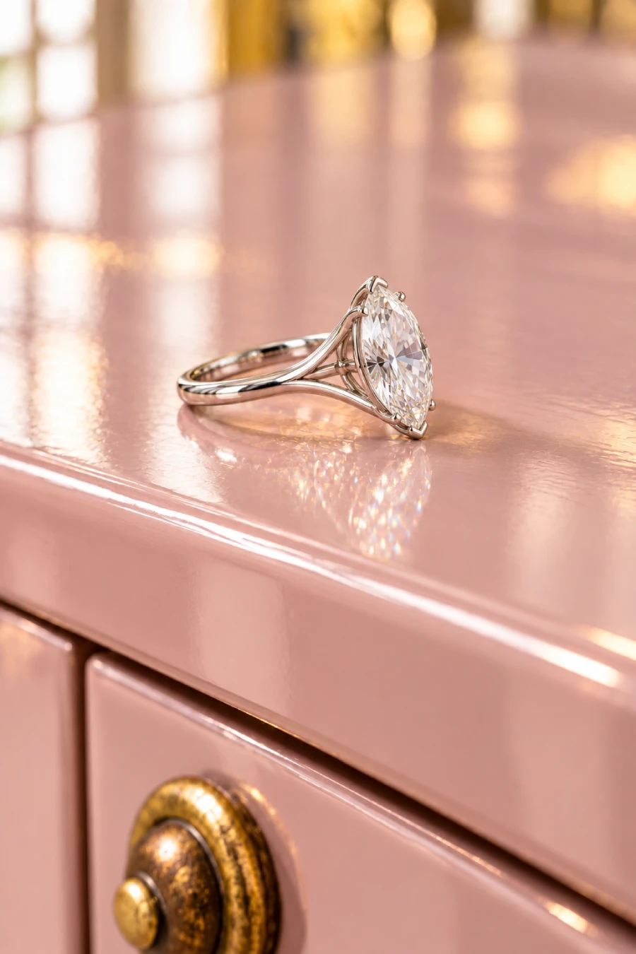 Marquise Engagement Rings: The Vintage Cut With Main-Stage Energy 14 Marquise diamond solitaire engagement ring with a split shank resting on a glossy blush pink dresser above a round brass knob