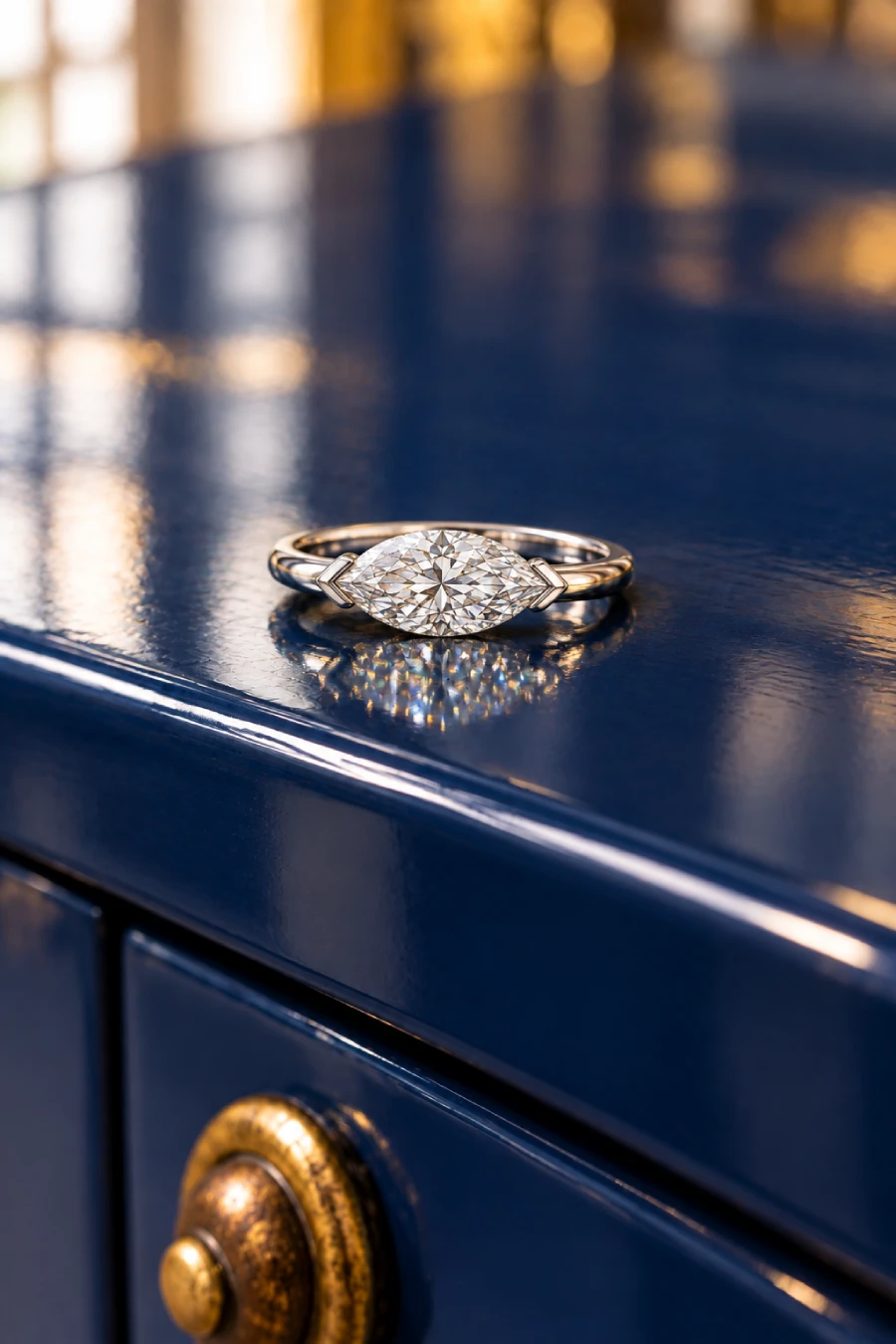 Marquise Engagement Rings: The Vintage Cut With Main-Stage Energy 13 East-west marquise diamond engagement ring with a polished band on a glossy navy blue dresser reflecting natural window light