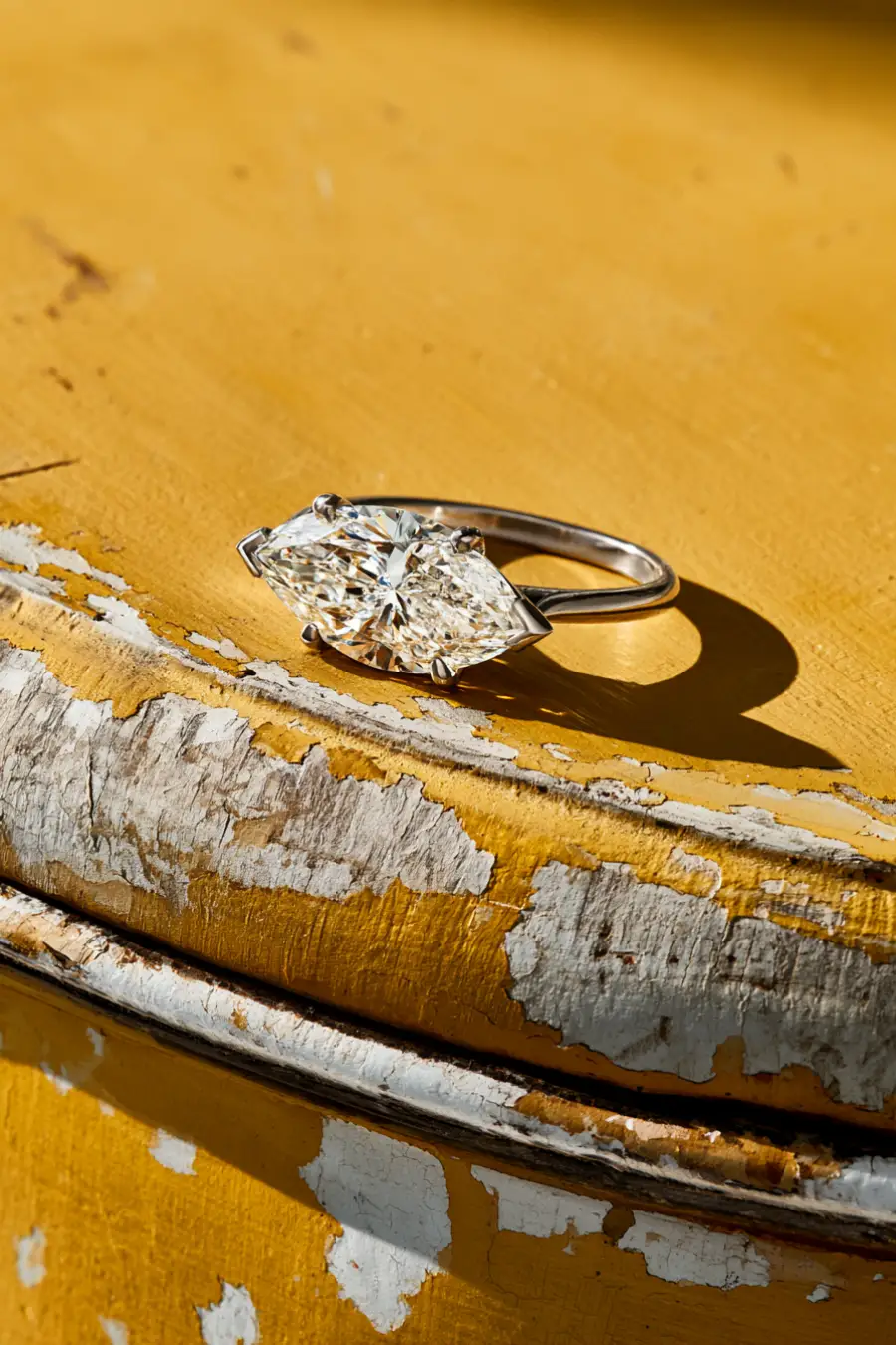 Marquise Engagement Rings: The Vintage Cut With Main-Stage Energy 2 East-west marquise diamond solitaire ring on distressed yellow and white wood, casting a defined shadow in afternoon sunlight
