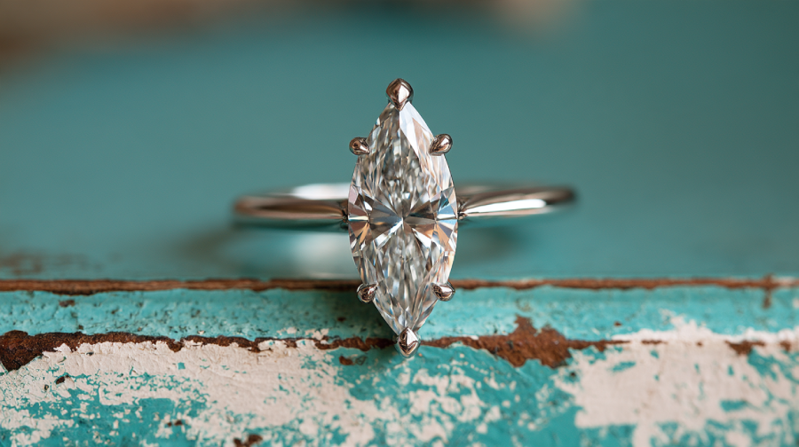 Close-up of a marquise diamond engagement ring with a slender silver band placed on distressed aquamarine and white wood edge